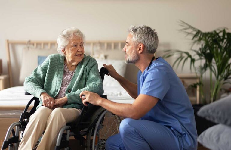 A small group of older adults smiling and talking together in a cozy, sunlit common room.